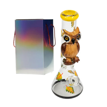 Glass smoking bong with owl design and colourful leaves, next to a rainbow-colored box.